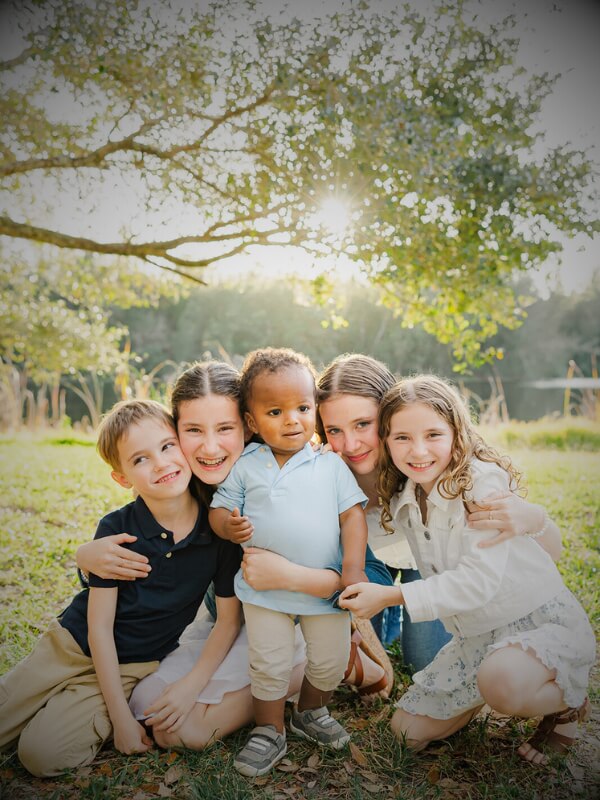 Small child with a family looking on outside on the grass with a lake in the background.